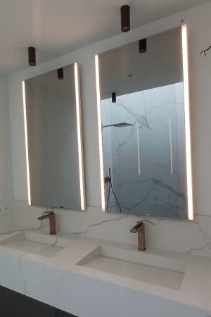Twee verlichte infraroodspiegels boven een dubbele wastafel in een strakke marmeren badkamer